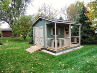 green cabin storage shed with a porch and brown doors for sale in vandalia ohio