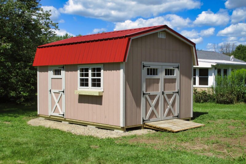 One of our highwall sheds for sale in Dublin OH - Peach siding white trimmed single and double doors and windows - red roof against a blue clouded sky on a sun-lit grassy yard