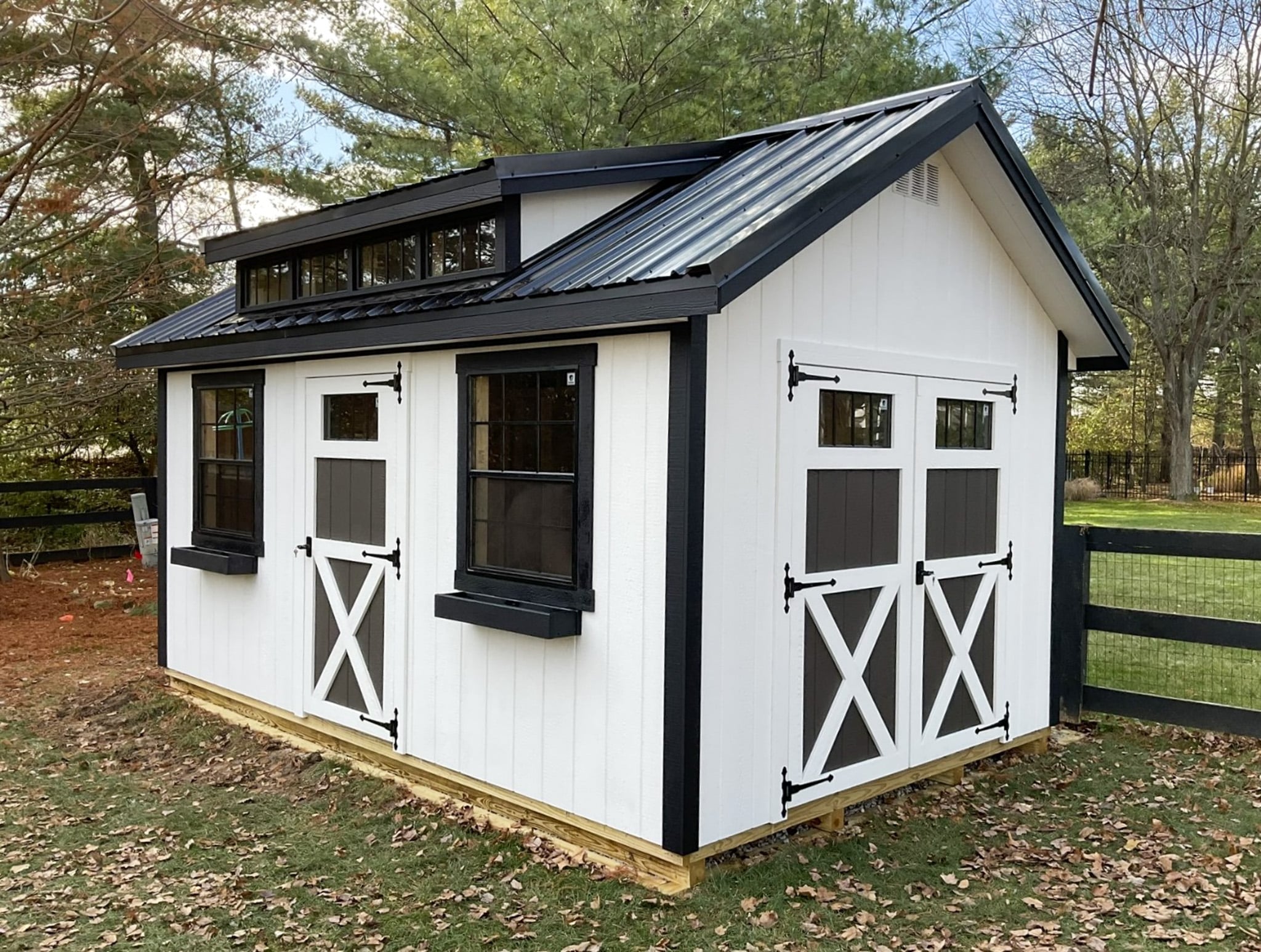 Black and white cottage-style shed with metal roof and double doors.